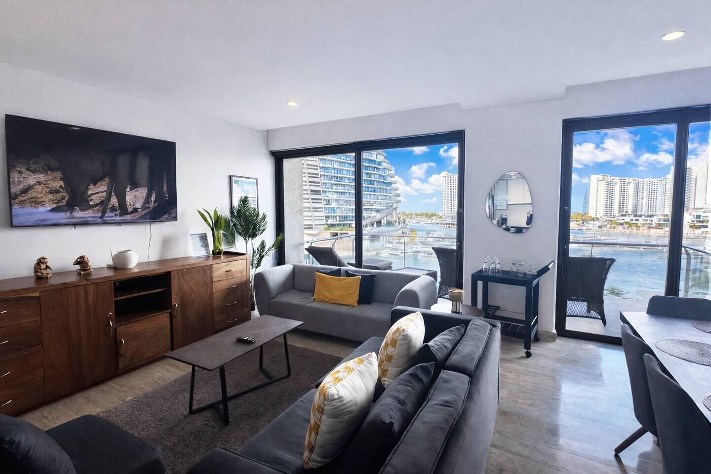 Un salon moderne avec un canapé, une table basse et un téléviseur. Il y a un balcon avec vue sur la ville.