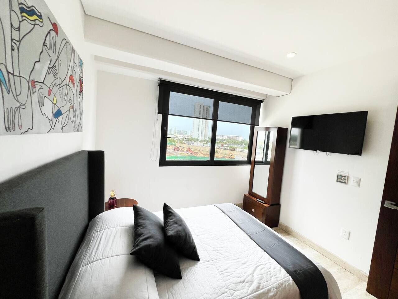 Une chambre à coucher comprenant un lit, une fenêtre, un téléviseur à écran plat et une œuvre d’art accrochée au mur.