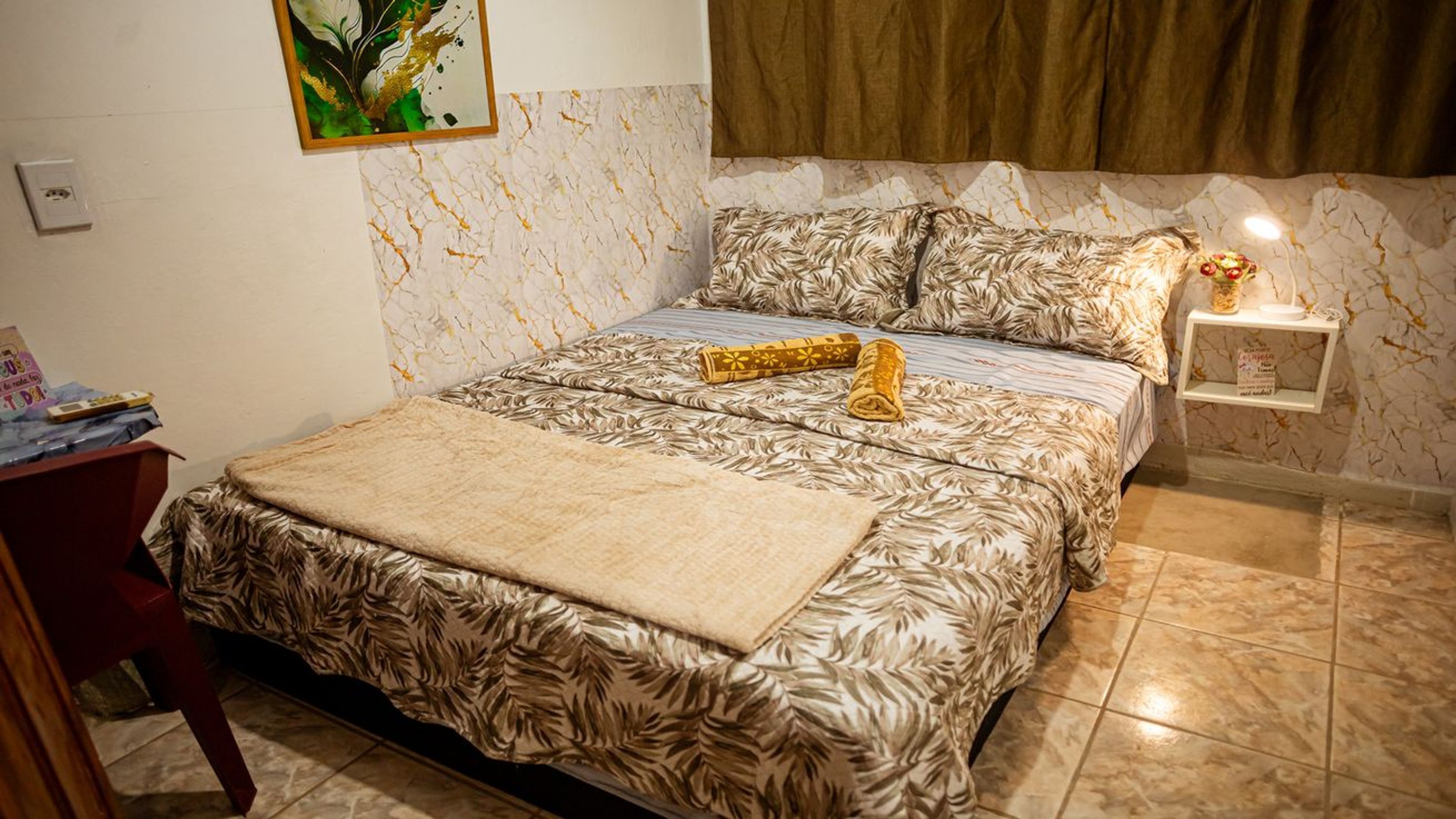 Un dormitorio con cama, mesita de noche, estante en la pared y un cuadro.