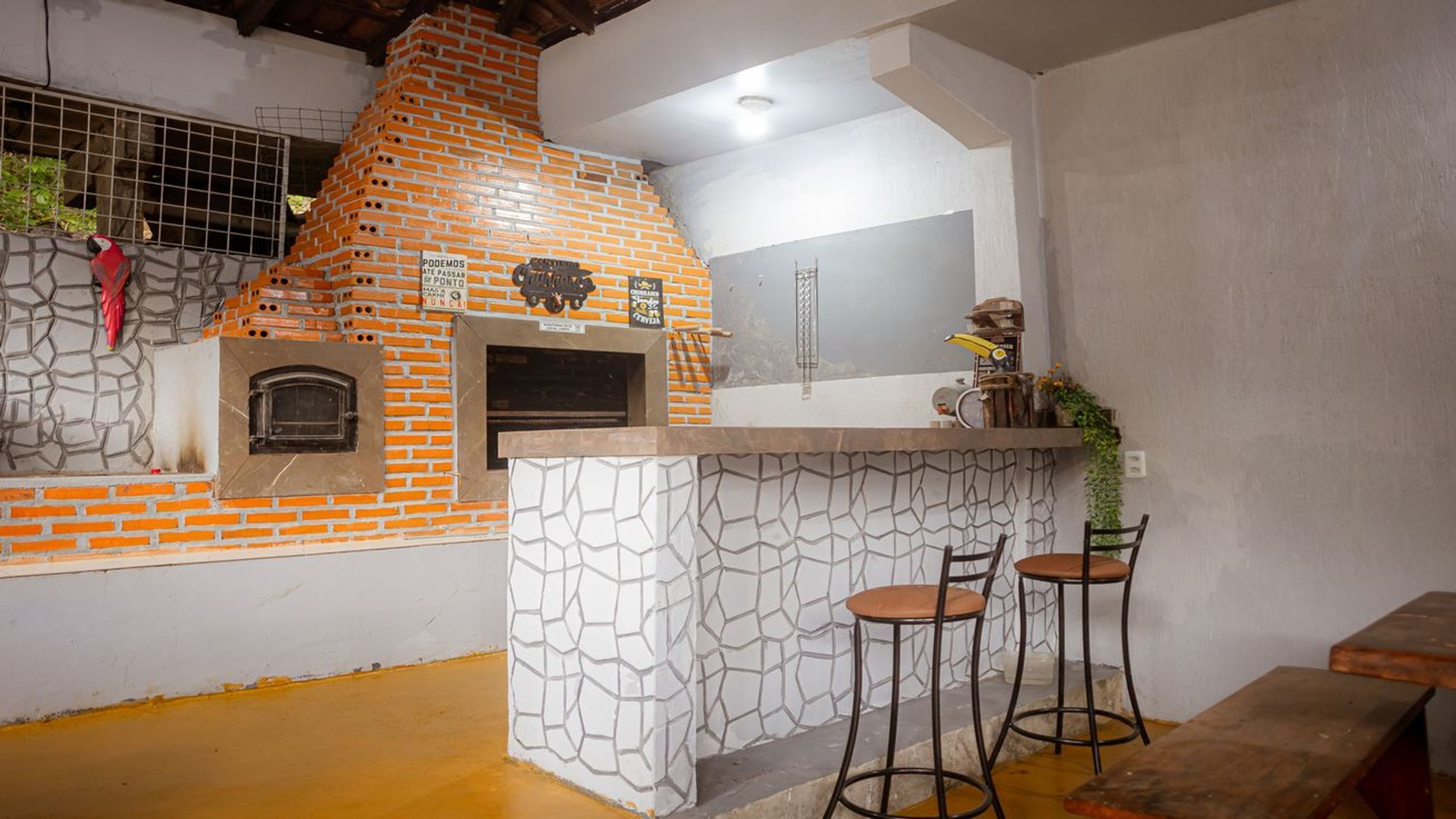 Una cocina con horno de ladrillo, barra con taburetes y ventana con celosía de metal.