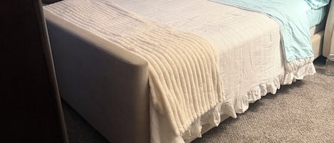 A bedroom with a bed, a chair, a bedside table, and a wall-mounted picture.