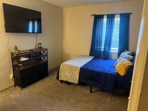 A bedroom with a bed, a TV mounted on the wall, a dresser, and a window with curtains. - 2-bedroom 2 bath apartment in pleasant Indianapolis with cool AC (Indianapolis)
