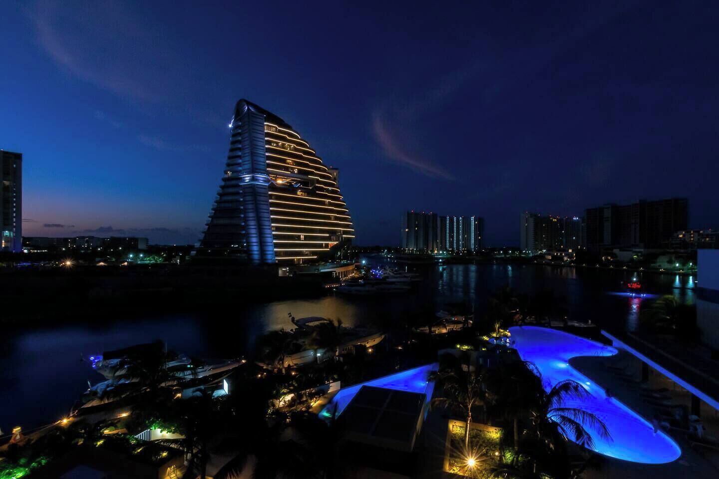 Ein modernes Hotel mit markanter, geschwungener Architektur, direkt an einem Ufer mit Pool und Marina gelegen.
