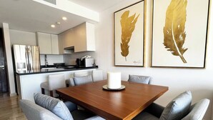 Et moderne spiseområde med et træbord og grå polstrede stole, et hvidt lysstagedesign og to billeder med fjer på væggen.