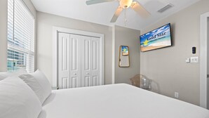 Une chambre d’hôtel avec un lit, un ventilateur de plafond, une télévision, une porte et une fenêtre avec des stores.