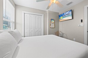 Ein Hotelzimmer mit Bett, Deckenventilator, Fernseher, Tür und Fenster mit Jalousien.