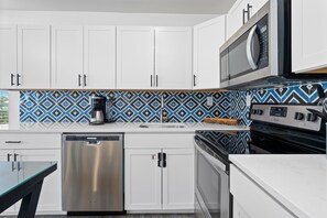 A modern kitchen with white cabinets, a stainless steel dishwasher, a microwave, and a patterned backsplash. - Full Home Duplex, Includes Both Sides w/ Private Pool Steps From Beach (Gulf Shores)