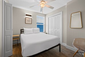 Une chambre à coucher comprenant un lit, un ventilateur de plafond, une fenêtre avec des stores, une porte et une chaise.