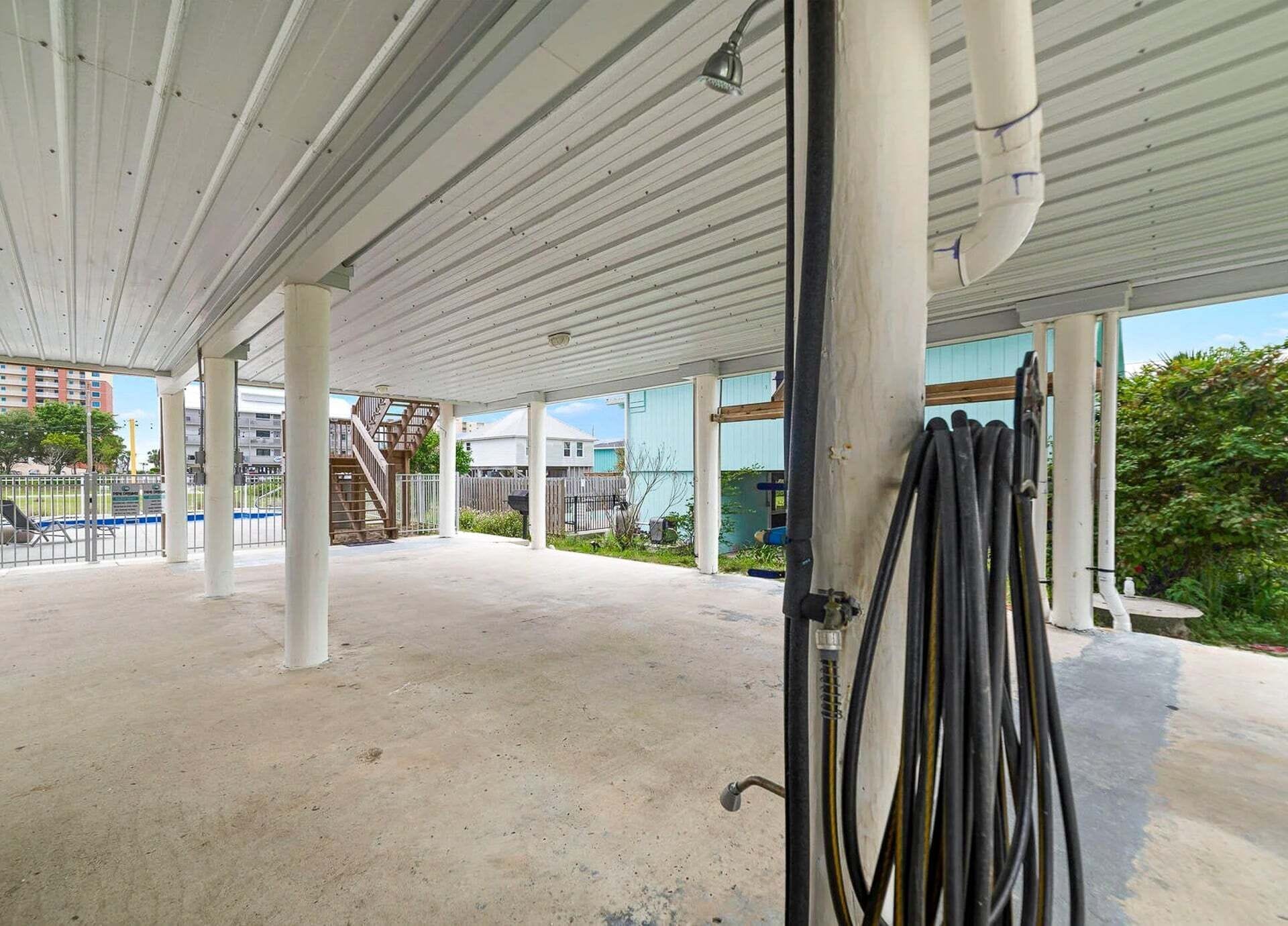 An outdoor covered parking area with concrete flooring, metal railings, and a staircase leading to a building.