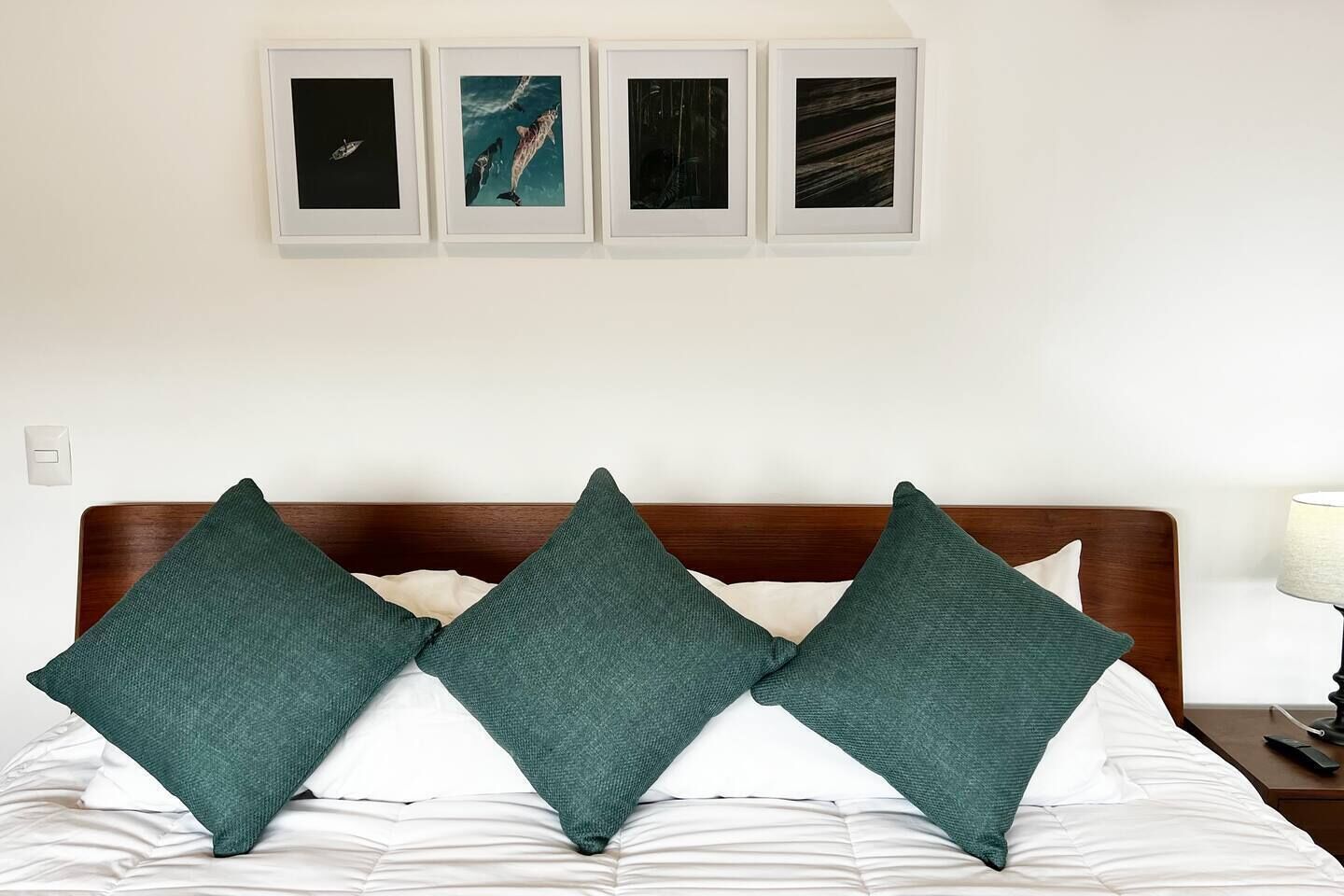 Un lit avec trois oreillers, une tête de lit en bois et quatre tableaux encadrés accrochés au mur.
