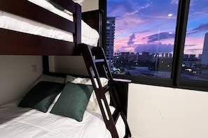 Una cama individual con vista a la ciudad al anochecer.