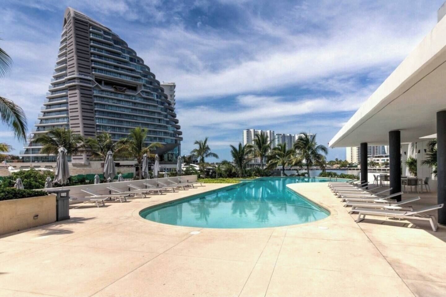 Ein Swimmingpool mit Liegestühlen, Palmen und modernen Gebäuden im Hintergrund.