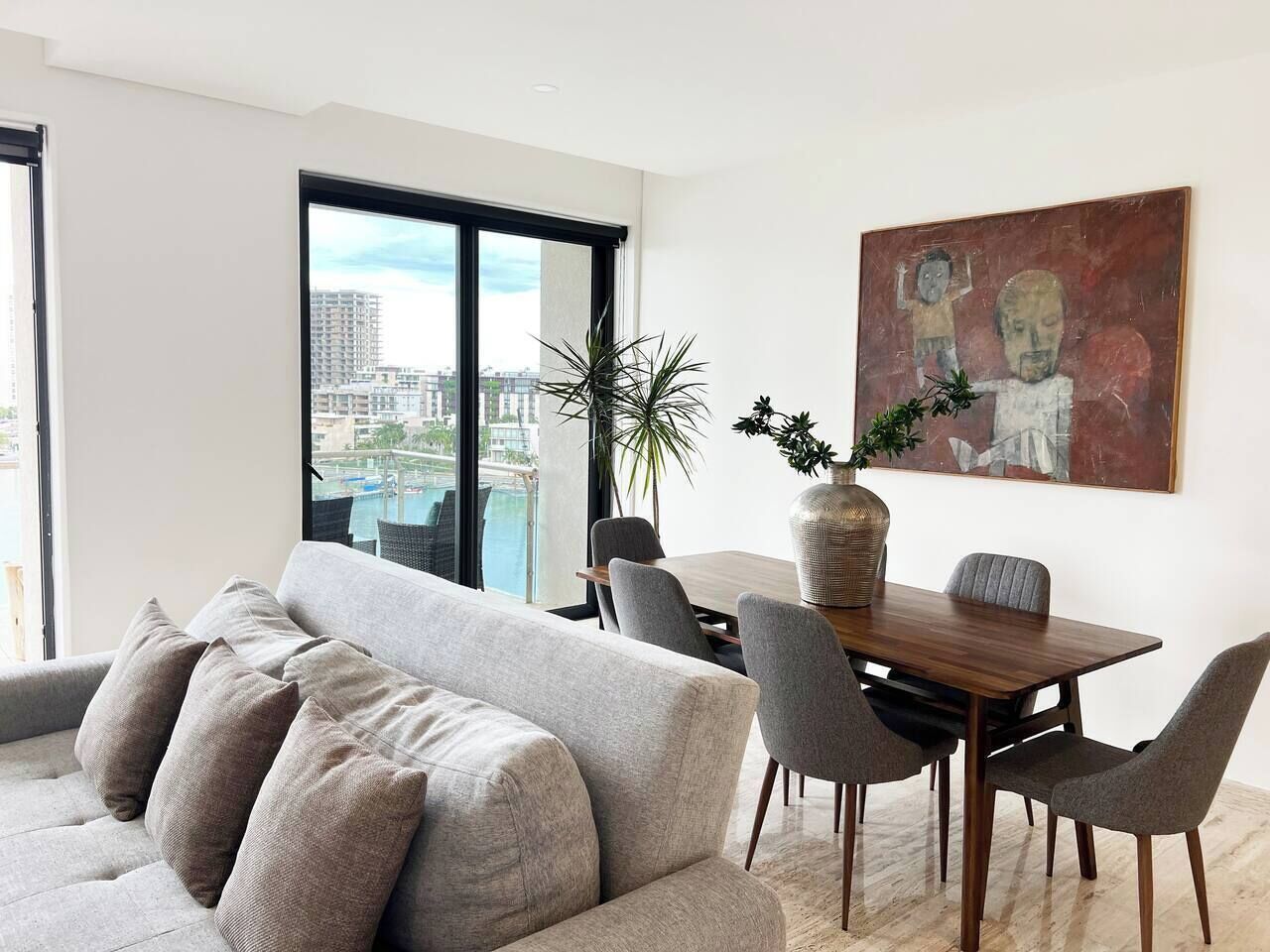 Ein modernes Wohnzimmer mit einer Couch, einem Esstisch, Stühlen, einem großen Fenster mit Blick auf die Stadt und einem Bild an der Wand.
