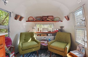 A compact living space with two green armchairs, a small table, and a shelf with various items. - The Country Manor | Historic Estate (Carpinteria)
