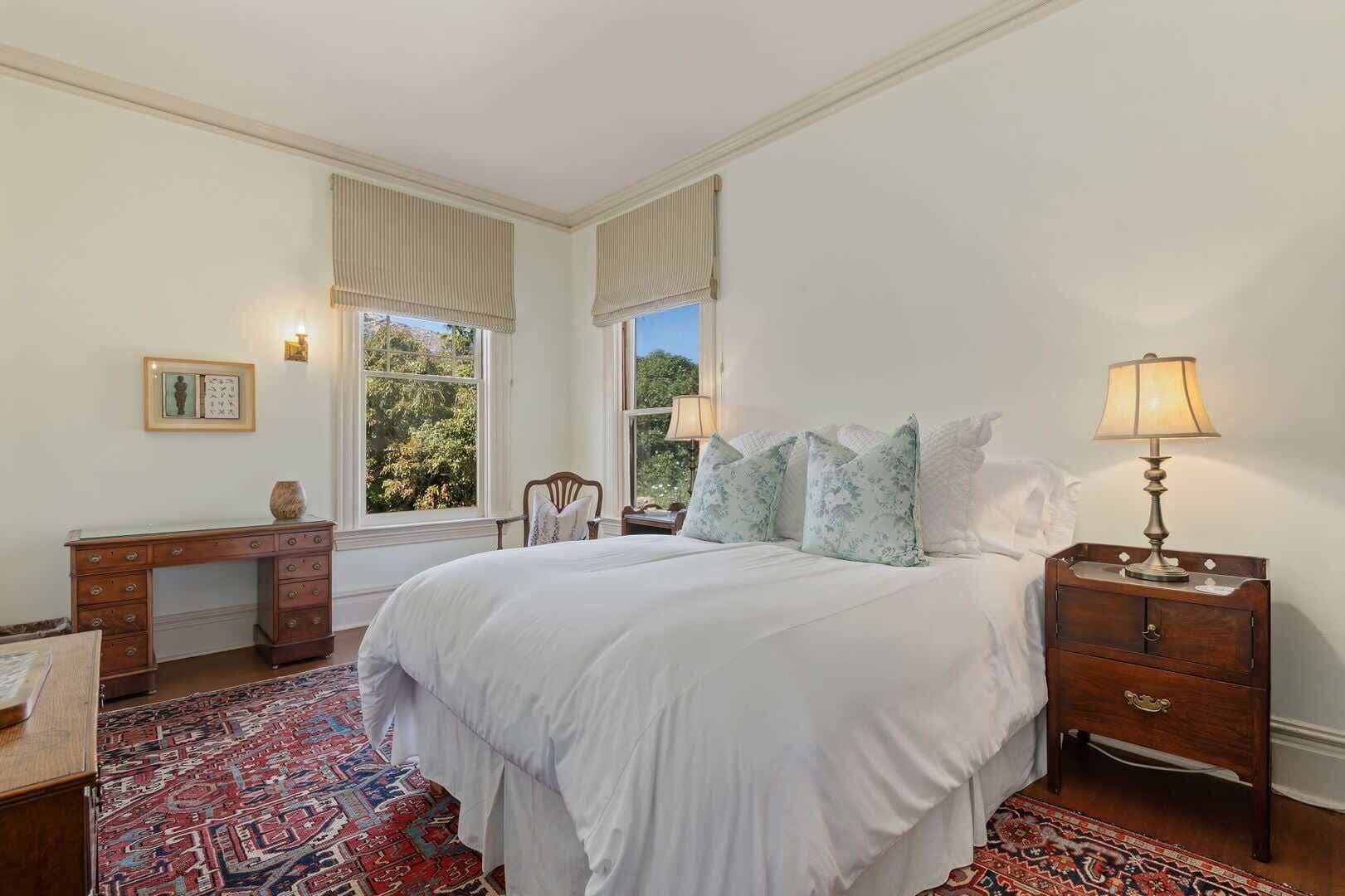 A bedroom with a large bed, a desk, and a nightstand with lamps.