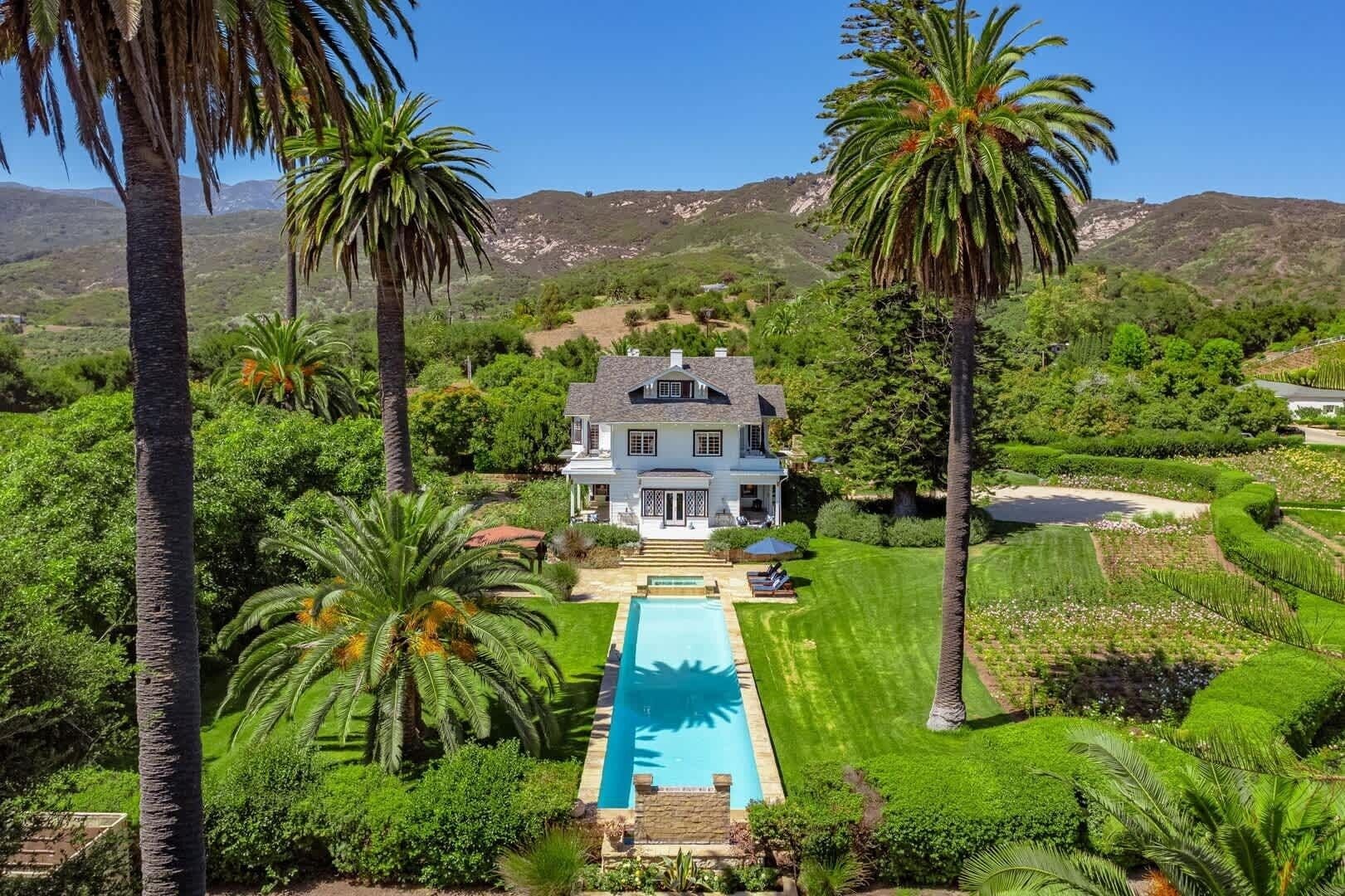 A large house with a swimming pool surrounded by lush greenery and palm trees.