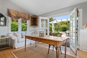A room with a wooden table, white sofa, and a view of greenery outside. - The Country Manor | Historic Estate (Carpinteria)