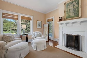 A room with a fireplace, two white sofas, a table with a lamp, and a painting on the wall. - The Country Manor | Historic Estate (Carpinteria)