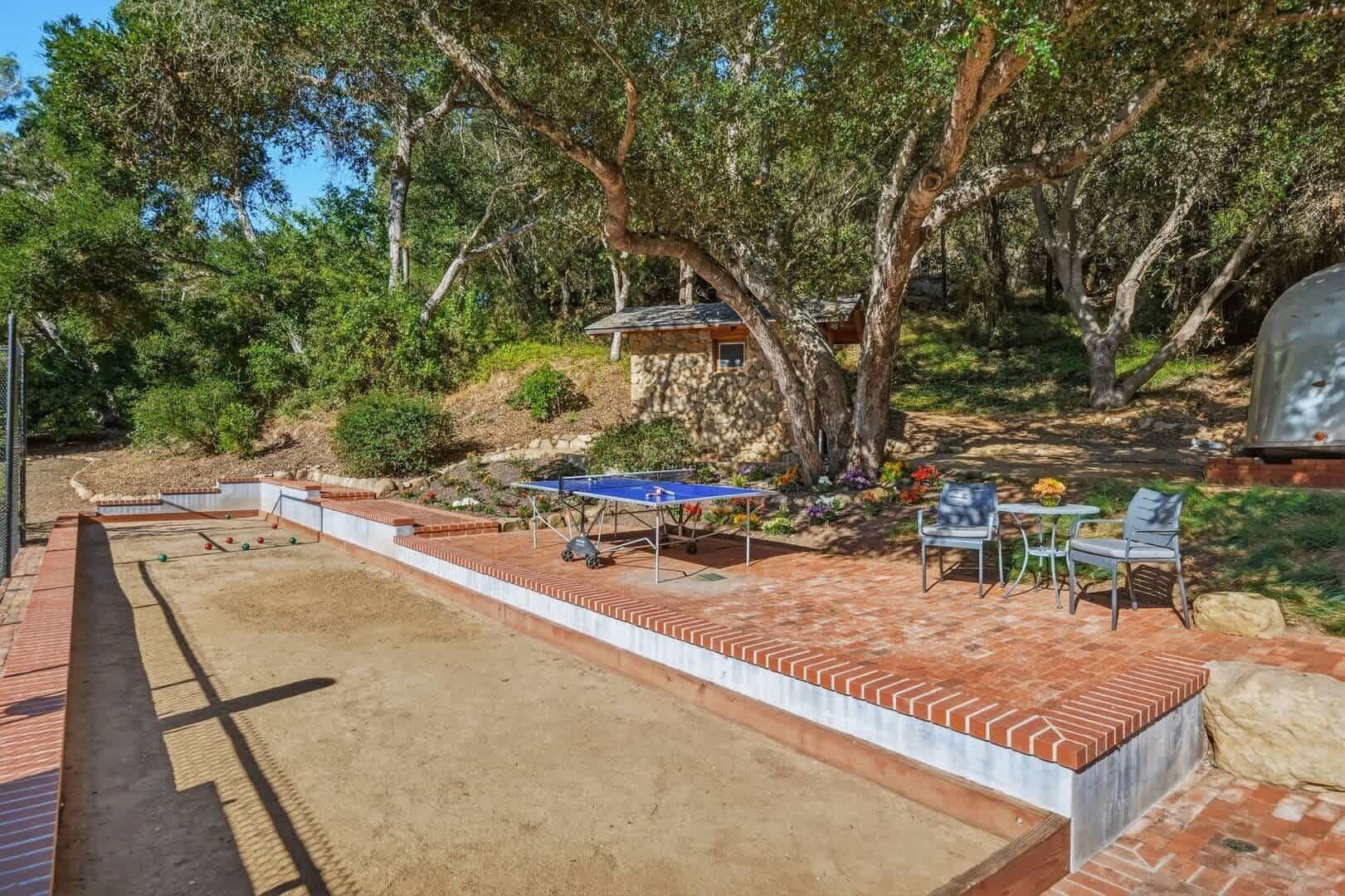 An outdoor recreational area with a ping pong table, seating, and a barbecue grill.