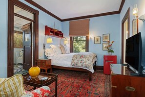A bedroom with a bed, bedside tables, a TV, a red cabinet, and a large window. - The Country Manor | Historic Estate (Carpinteria)