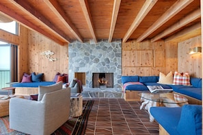 A cozy interior with a stone fireplace, wooden beams, and blue upholstered seating. - Montecito Pointe (Summerland)
