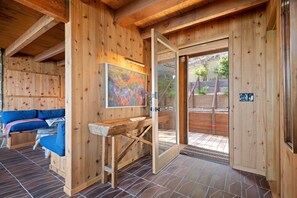 A wooden interior with a sofa, a painting, and a door leading outside. - Montecito Pointe (Summerland)