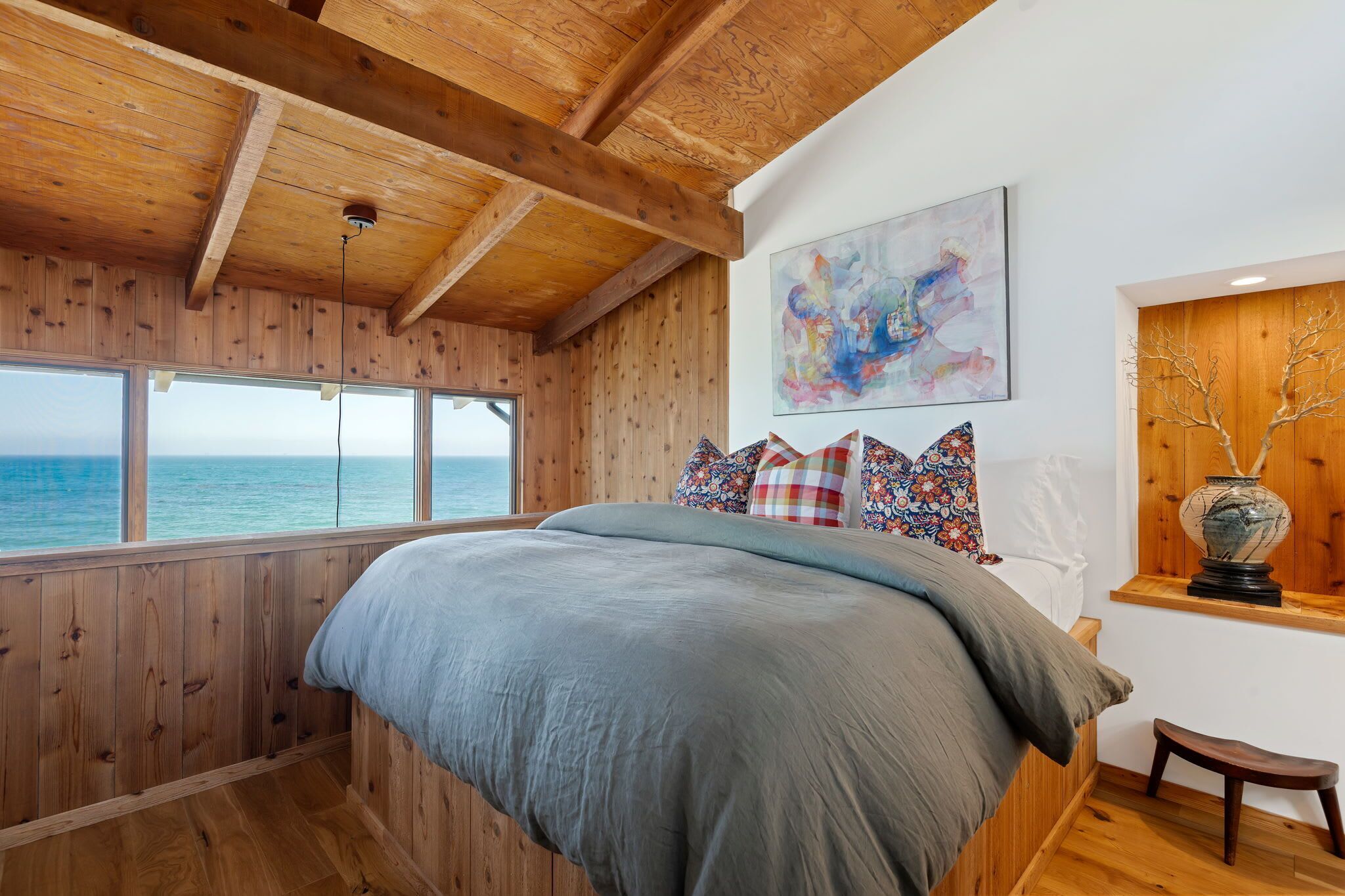 Ein Schlafzimmer mit einem großen Bett, Holzwänden, Blick auf das Meer und einem Gemälde an der Wand.
