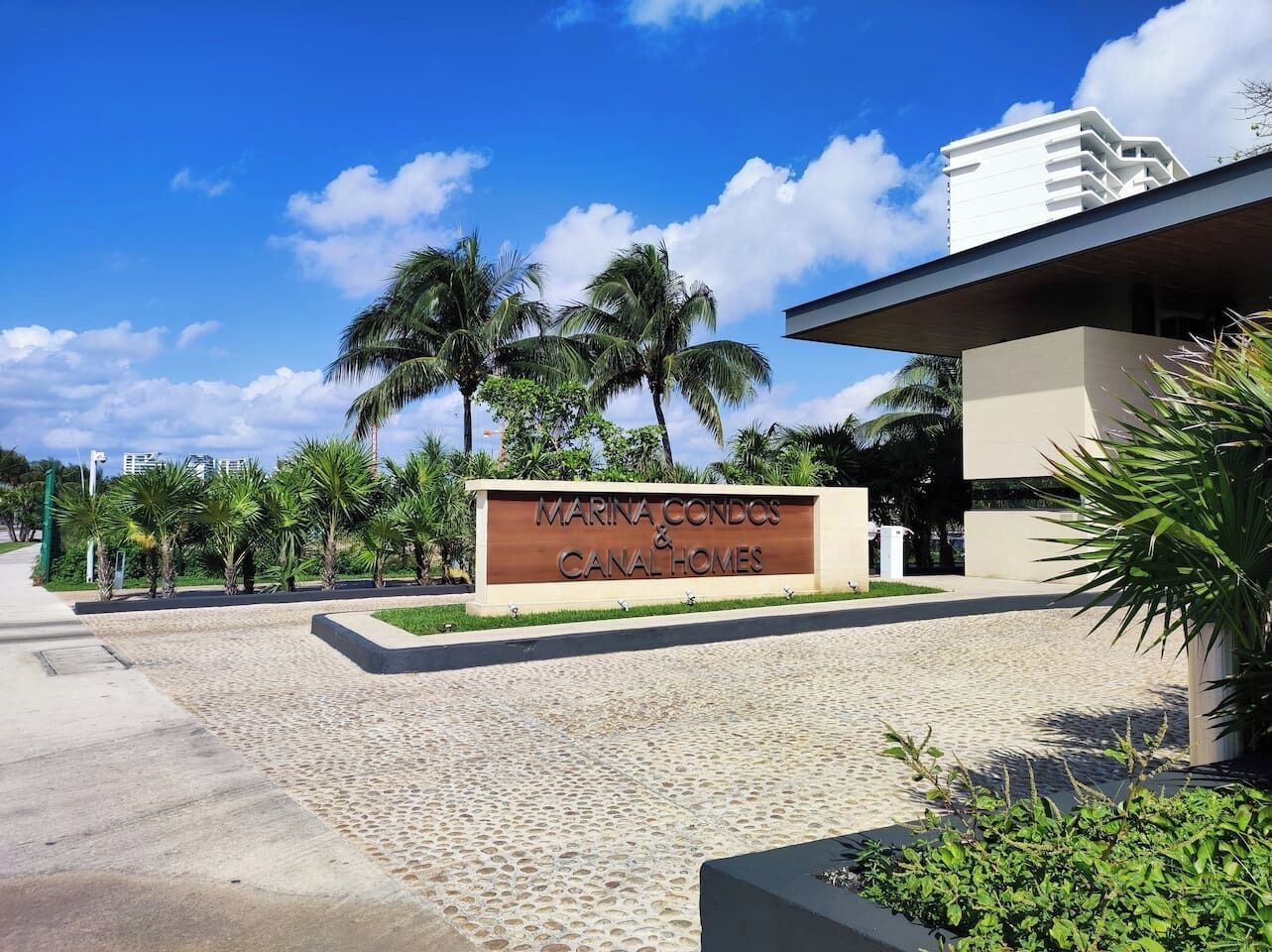Señal de Marina Condos & Canal Homes con un camino pavimentado y palmeras.