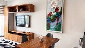A modern living room with a flat-screen TV, wooden entertainment unit, dining table, and chairs. - TOP/ 1BR/Luxury Condo/ Ocean/Marina/Canal Views/HZ (Cancún)