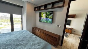 A bedroom with a bed, a TV mounted on the wall, a wooden cabinet, and a view of the outside through a window. - TOP/ 1BR/Luxury Condo/ Ocean/Marina/Canal Views/HZ (Cancún)