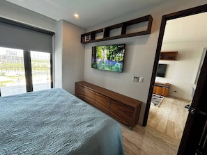 Un dormitorio con cama, televisor montado en la pared, mueble de madera y vista al exterior a través de una ventana.
