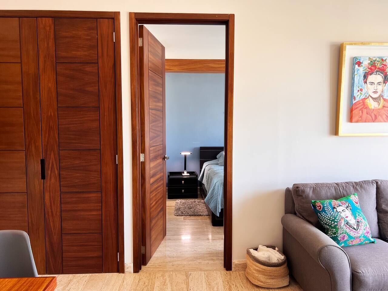 Une pièce comprenant une armoire en bois, un canapé gris agrémenté d’un coussin décoratif et un lit recouvert d’une couverture bleue.