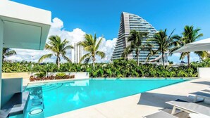 A swimming pool with lounge chairs, surrounded by palm trees and a modern building in the background. - TOP/ 1BR/Luxury Condo/ Ocean/Marina/Canal Views/HZ (Cancún)