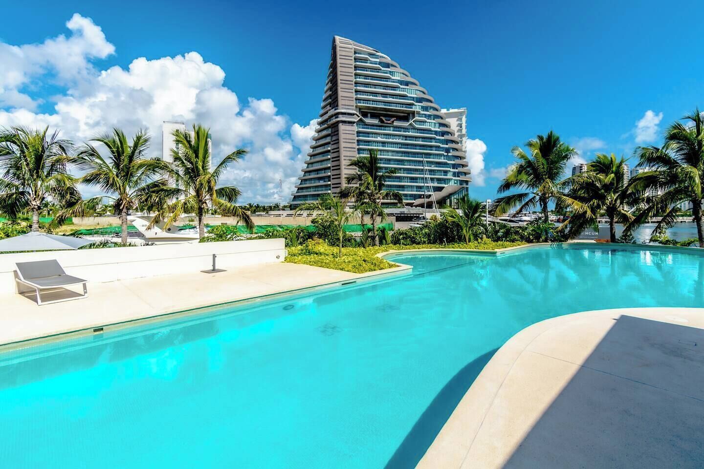 Un hotel con un edificio moderno, piscina y palmeras.