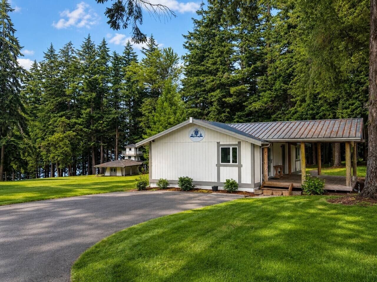 A small, single-story building with a porch, surrounded by a well-maintained lawn and tall trees.