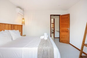 Een hotelkamer met een bed, een houten hoofdeinde, een wandairconditioner en een houten deur.