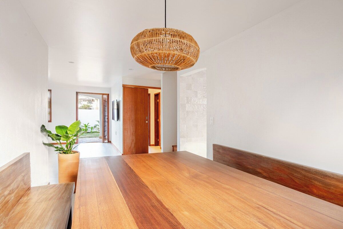Ein modernes Interieur mit einem langen Holztisch, einer hängenden Korbschaukel-Lampe und einem Topfpflanzen.