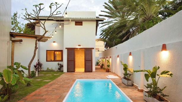 A rectangular swimming pool with a tiled deck, surrounded by potted plants and a white wall. - Mar Stays - House 22A (Salvador)