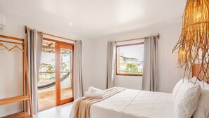 A hotel room with a bed, a wooden shelf, a hammock, and a view of the outside. - Mar Stays - House 22A (Salvador)