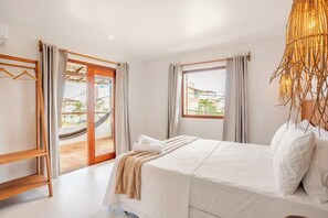 Une chambre d’hôtel avec un lit, une étagère en bois, un hamac et une vue sur l’extérieur.