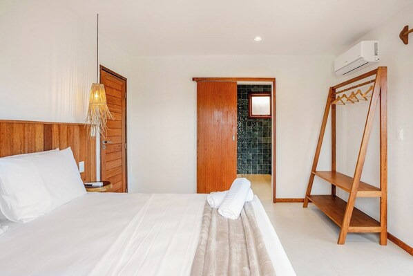 Habitació d'hotel amb un llit, un armari de fusta, una làmpada penjant, una prestatgeria de fusta i un aparell d'aire condicionat.