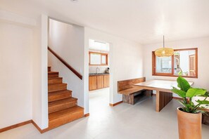 Un interior moderno con una escalera, un comedor con un banco y una cocina al fondo.