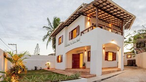 A two-story house with a covered porch, a front door, and a small garden area. - Mar Stays - House 22A (Salvador)
