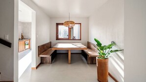 A modern interior with a dining area featuring a wooden table and benches, a hanging light fixture, and a potted plant. - Mar Stays - House 22A (Salvador)