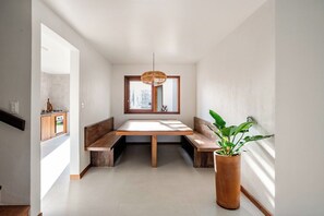 Un intérieur moderne avec un coin repas comprenant une table et des bancs en bois, un luminaire suspendu et une plante en pot.