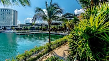 Un hotel frente al mar con piscina, palmeras y vista al horizonte de la ciudad.