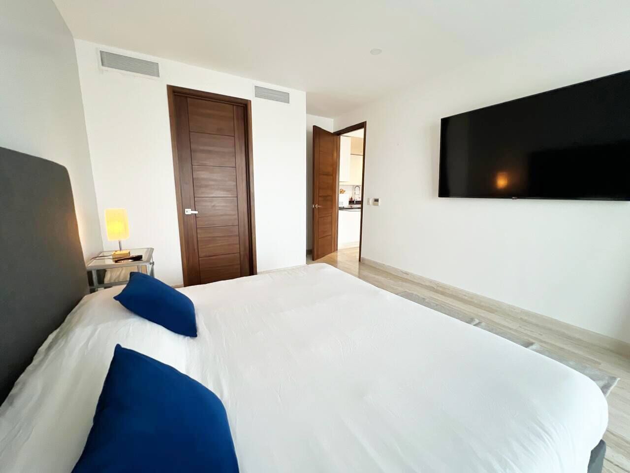 Ein Hotelzimmer mit Bett, einem an der Wand befestigten Fernseher, einer Tür und einer Lampe auf einem Nachttisch.