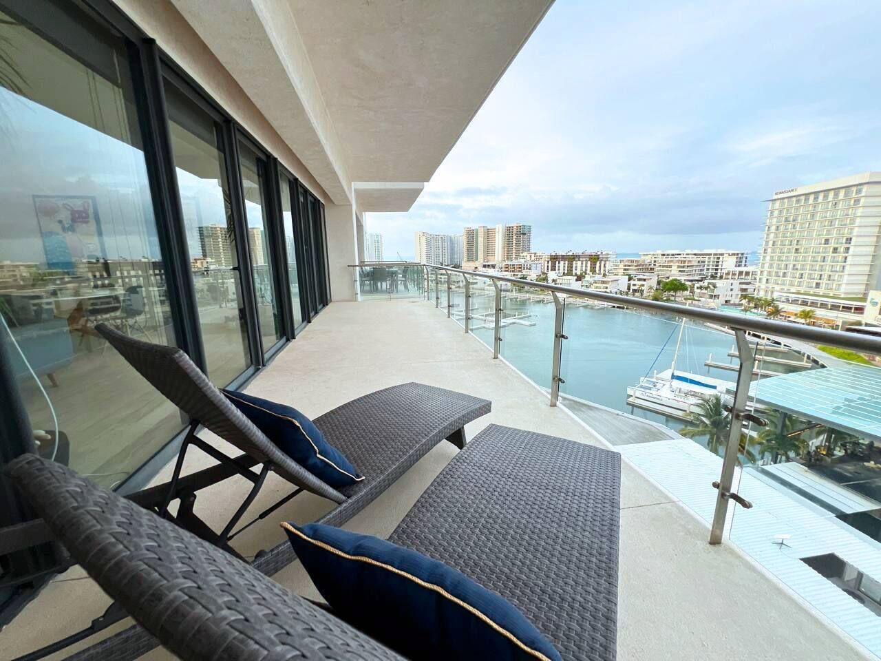 Ein Balkon mit zwei Loungesesseln, einer Glastrennwand und Blick auf einen Yachthafen mit Booten.