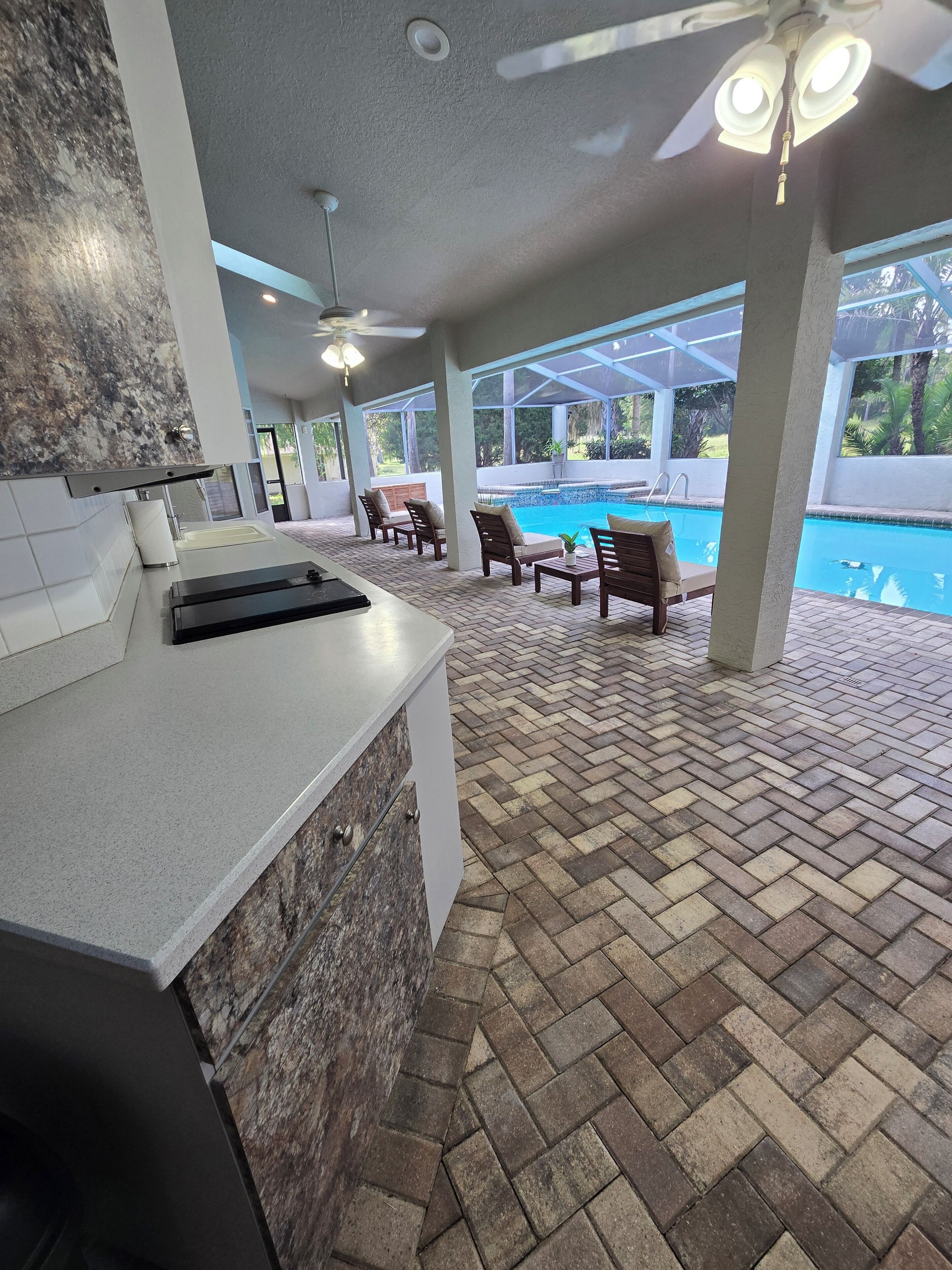 A poolside area with a kitchen counter, outdoor seating, and a ceiling fan.