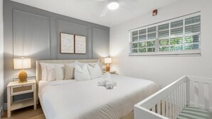 Ein Schlafzimmer mit Bett, Nachttischen, einem Fenster mit Jalousien und einem Deckenventilator.